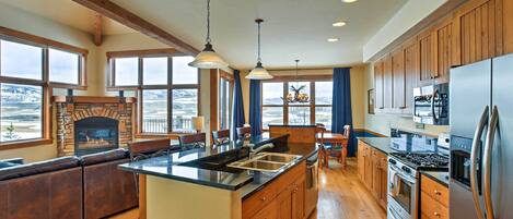 A spacious kitchen with wooden cabinets, a large island, and a stone fireplace.
