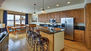 A kitchen with wooden cabinets, a stainless steel refrigerator, a large island with bar stools, and a dining area with a table and chairs. - Mtn-view Gem w/ On-site Golf! 3 Mi to Granby Ranch (Granby)