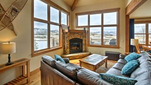 A cozy living room with a stone fireplace, leather sofa, and large windows offering a view of a snowy landscape. - Mtn-view Gem w/ On-site Golf! 3 Mi to Granby Ranch (Granby)