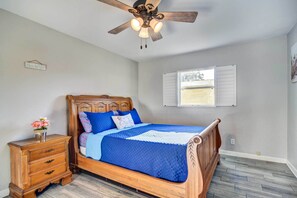 A bedroom with a wooden bed, a nightstand, a ceiling fan, and a window with shutters.