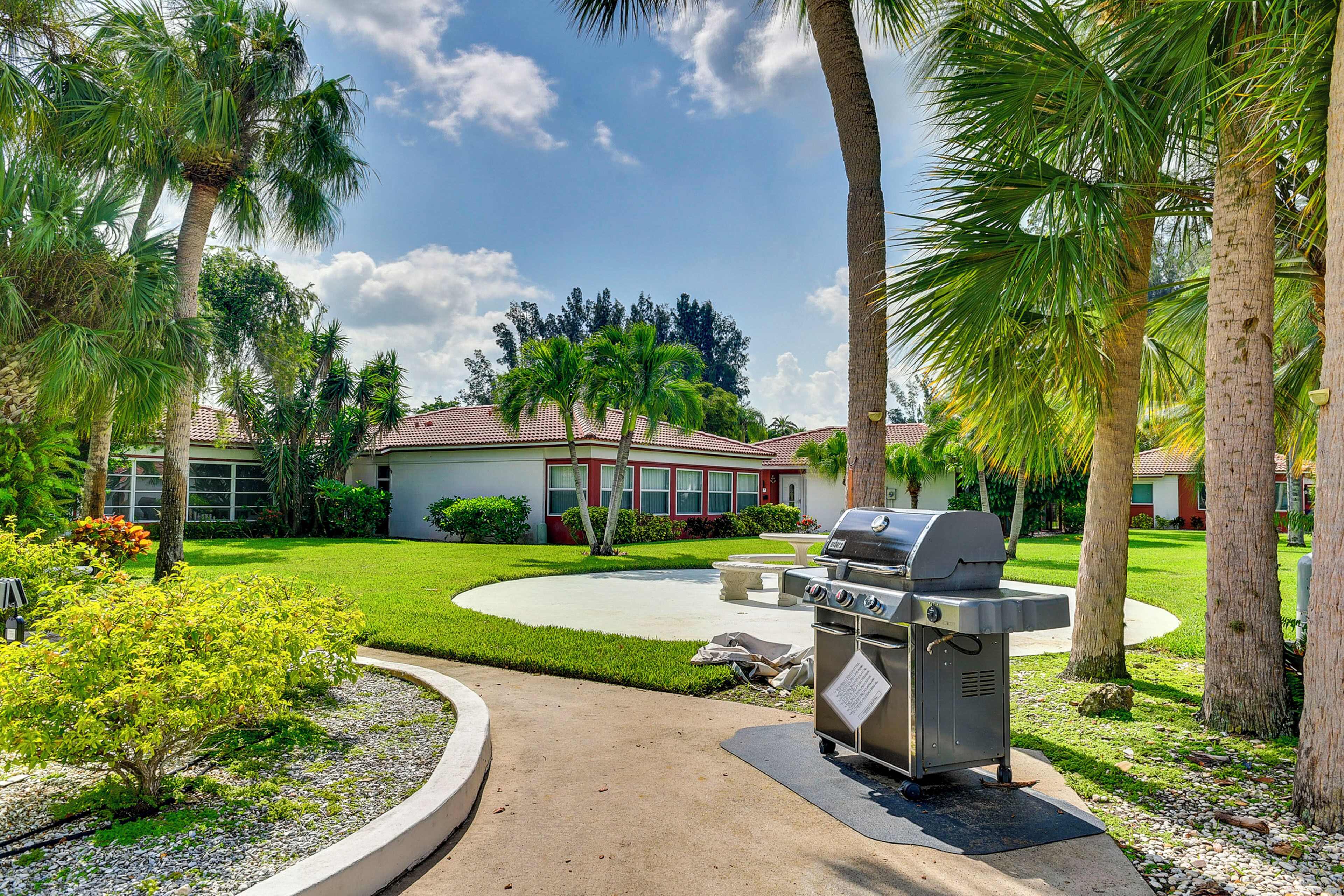 A backyard with a barbecue grill, palm trees, and a house with a red roof.