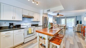 Une cuisine moderne avec des meubles blancs, un îlot central et un coin repas comprenant une table et des chaises en bois.