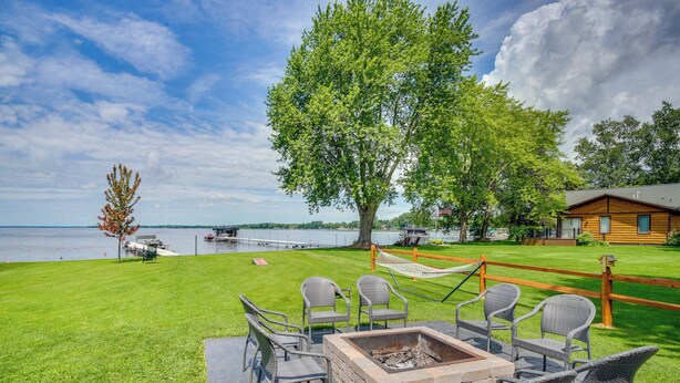 A patio with wicker chairs, a fire pit, and a view of a lake. - Bright Shawano Lake Oasis - Walk to Boat Launch! (Cecil)