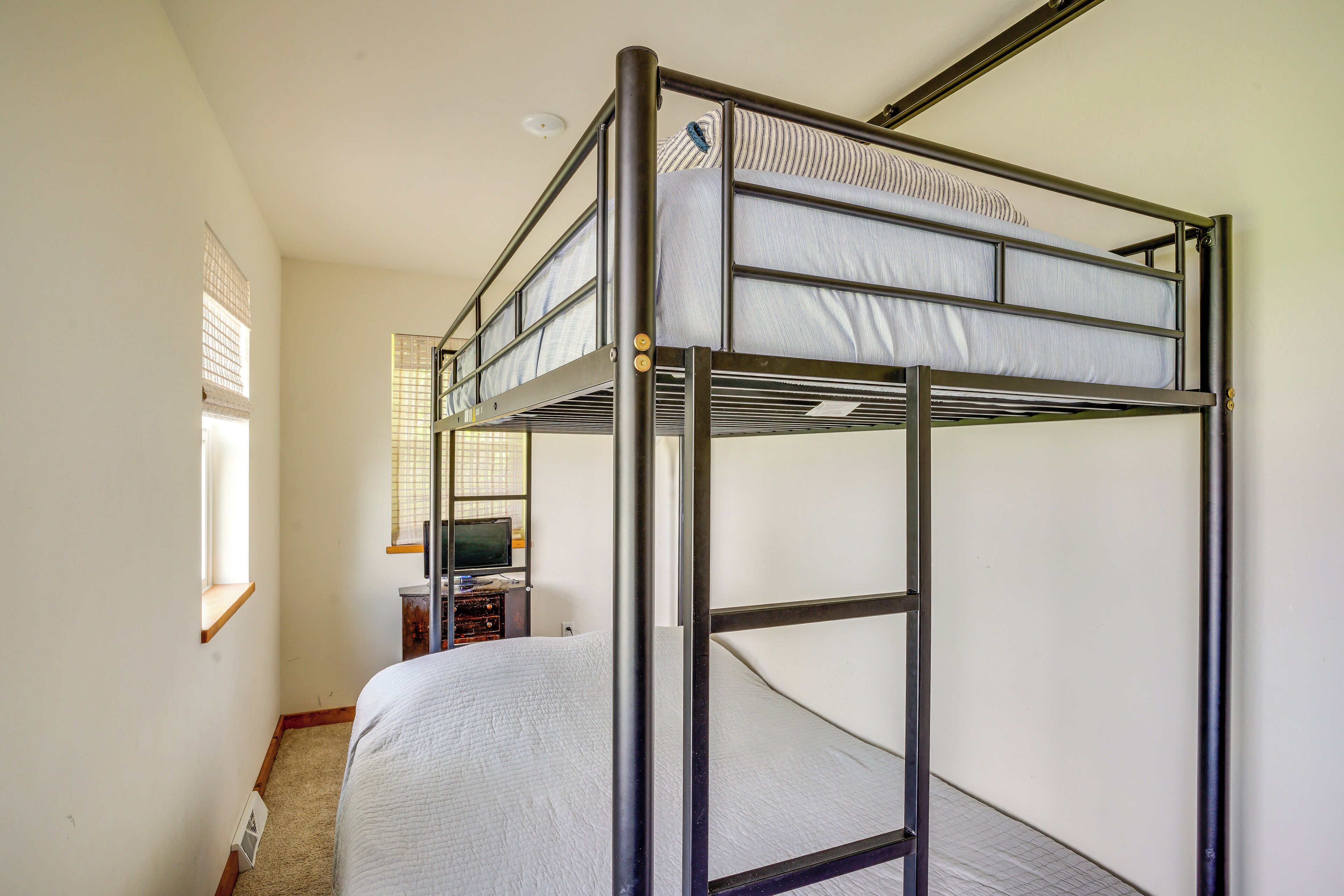 A bunk bed with a desk and chair, a window with blinds, and a small shelf.