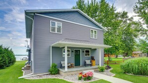A two-story house with a covered porch, a green door, and a small garden with flowers and shrubs. - Bright Shawano Lake Oasis - Walk to Boat Launch! (Cecil)