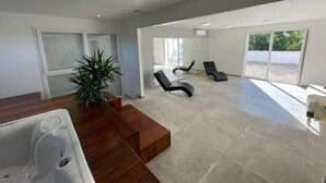 A spacious room with a wooden bench, a large window, and a jacuzzi tub. - Le Petit Millenium Avec SPA et Piscine (Saint-Alban-Auriolles)