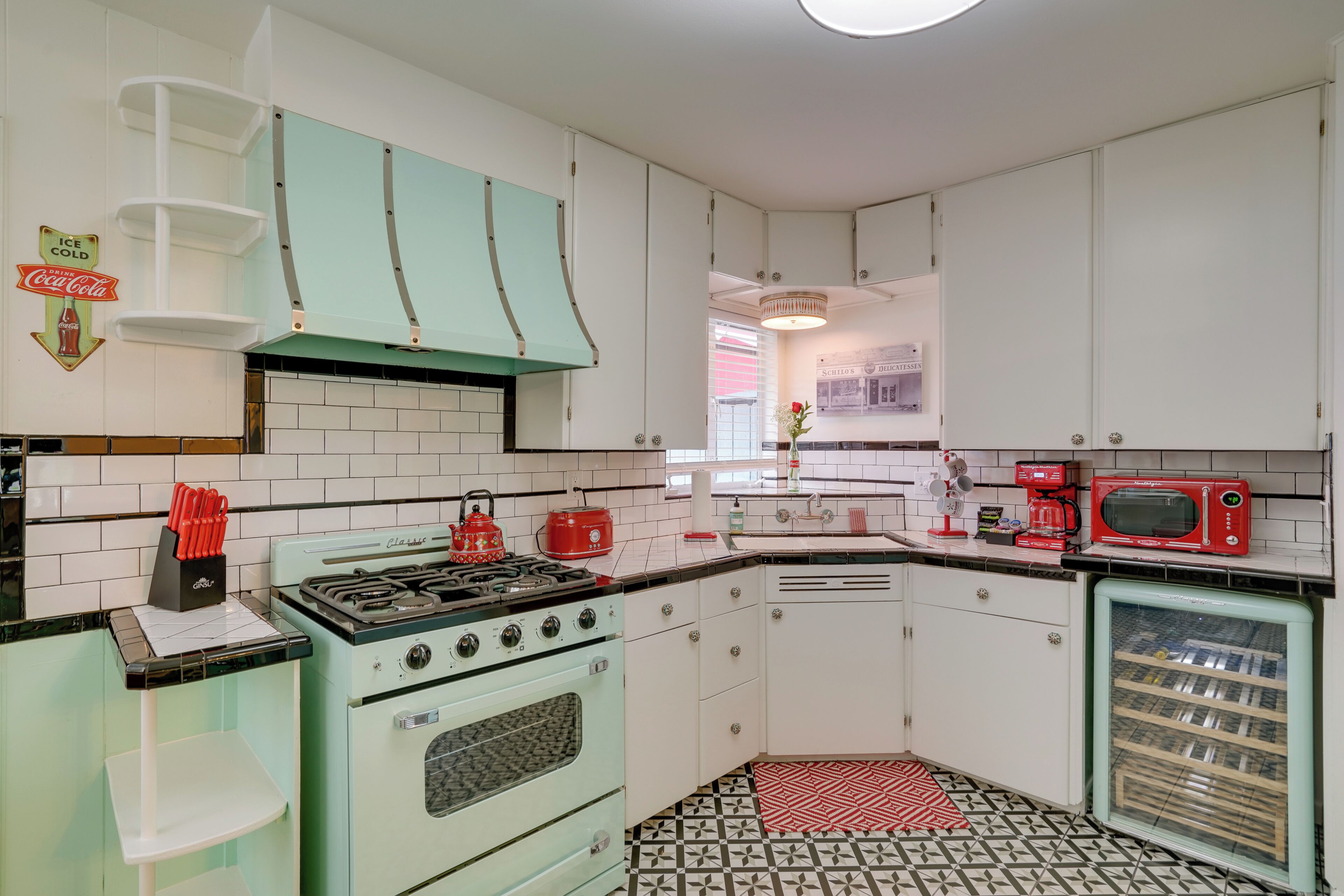 Una cocina de estilo retro con armarios blancos, una estufa verde y un microondas rojo.