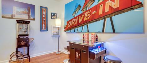 A bar area with a vintage jukebox, a neon sign, and a large painting of buildings.