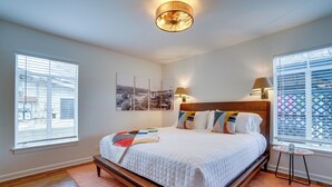 Ein Schlafzimmer mit einem großen Bett, zwei Nachttischlampen, einem kleinen Tisch und Blick ins Freie durch das Fenster.