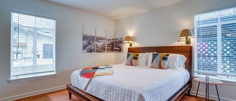 A bedroom with a large bed, two bedside lamps, a small table, and a view of the outside through the window.