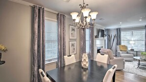 A dining area with a dark wooden table, white chairs, and a chandelier.