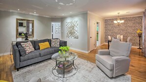 A living room with a grey sofa, a glass coffee table, and a grey armchair. There is a wall with a patterned wallpaper and a chandelier.