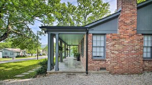 A covered porch with a gravel driveway leading to a brick building with a chimney.