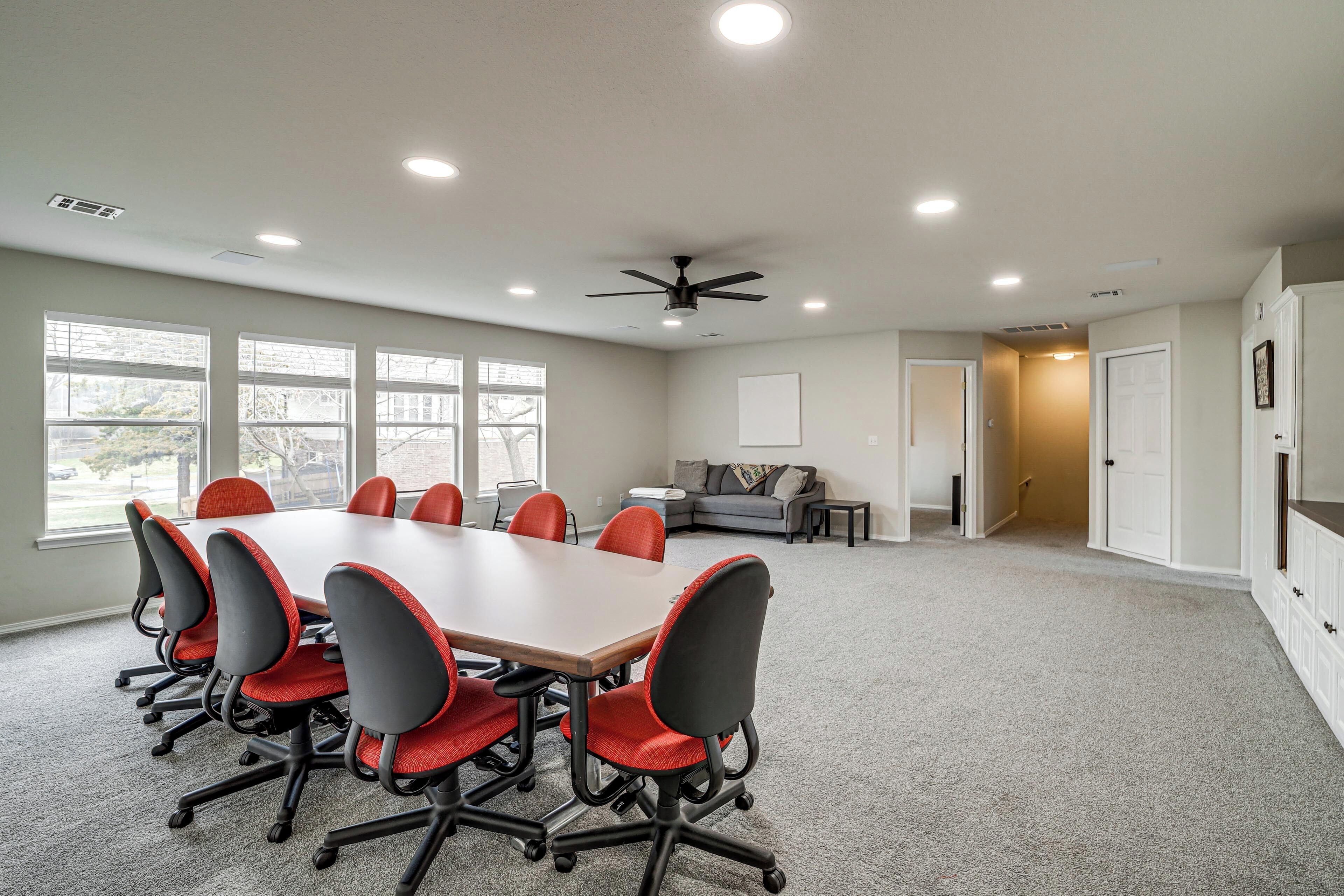 Une salle de conférence équipée d’une grande table, de six chaises, d’un ventilateur de plafond et de grandes fenêtres.