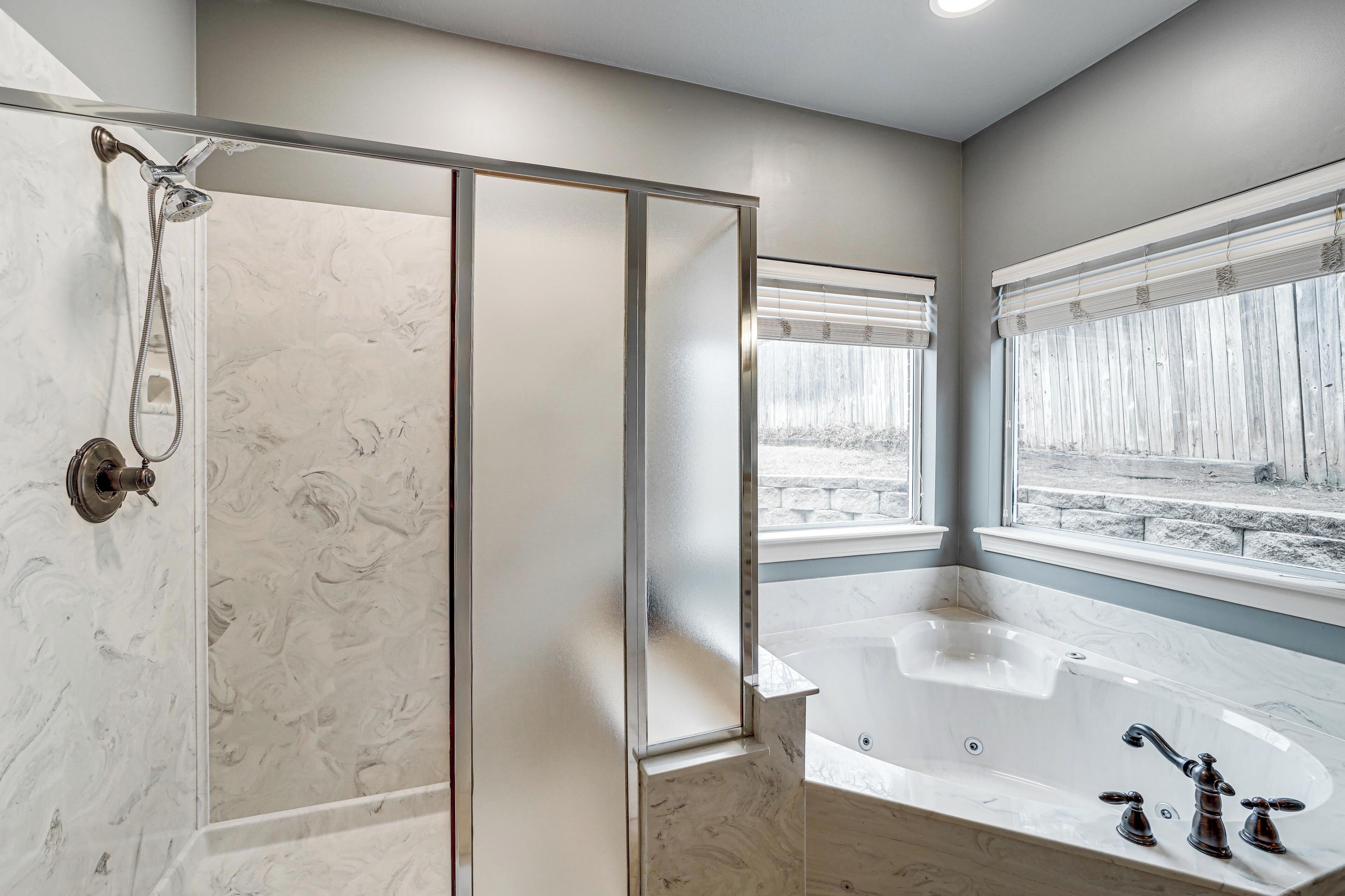 A modern bathroom with a glass-enclosed shower, a large bathtub, and a window providing a view of the outdoors.