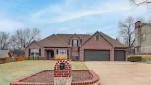 A two-story brick house with a stone fireplace, a garage, and a well-maintained lawn. - Pet-friendly Tulsa Escape w/ Private Hot Tub! (Tulsa)