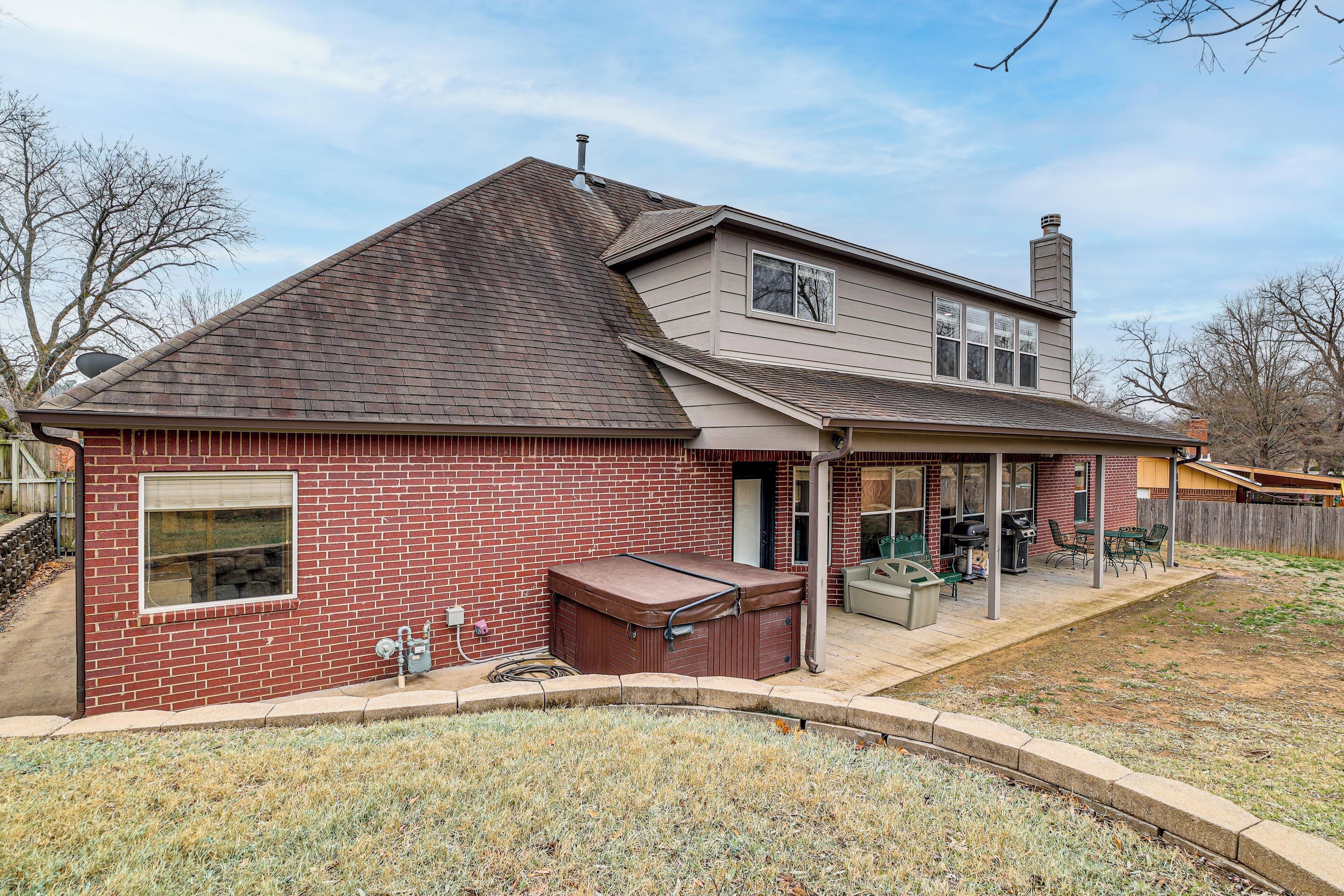 A two-story house with a brick exterior, a covered patio with outdoor furniture, and a hot tub.