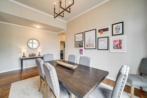 Ein Esszimmer mit einem dunklen Holztisch, grau gepolsterten Stühlen, einem runden Spiegel und gerahmten Bildern an der Wand.