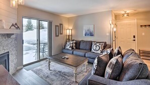A modern living room with a fireplace, a sofa set, a coffee table, and a large window with a view of snow outside. - Frisco Condo w/ 2 Hot Tubs: Steps to Lake Dillon (Frisco)