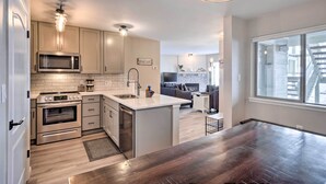 A modern kitchen with stainless steel appliances, a central island, and a dining area with a large window. - Frisco Condo w/ 2 Hot Tubs: Steps to Lake Dillon (Frisco)