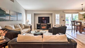 A modern living room with a fireplace, leather sofas, a glass coffee table, and a dining area with a chandelier. - Large Yard + Hot Tub: Reno Retreat! (Reno)