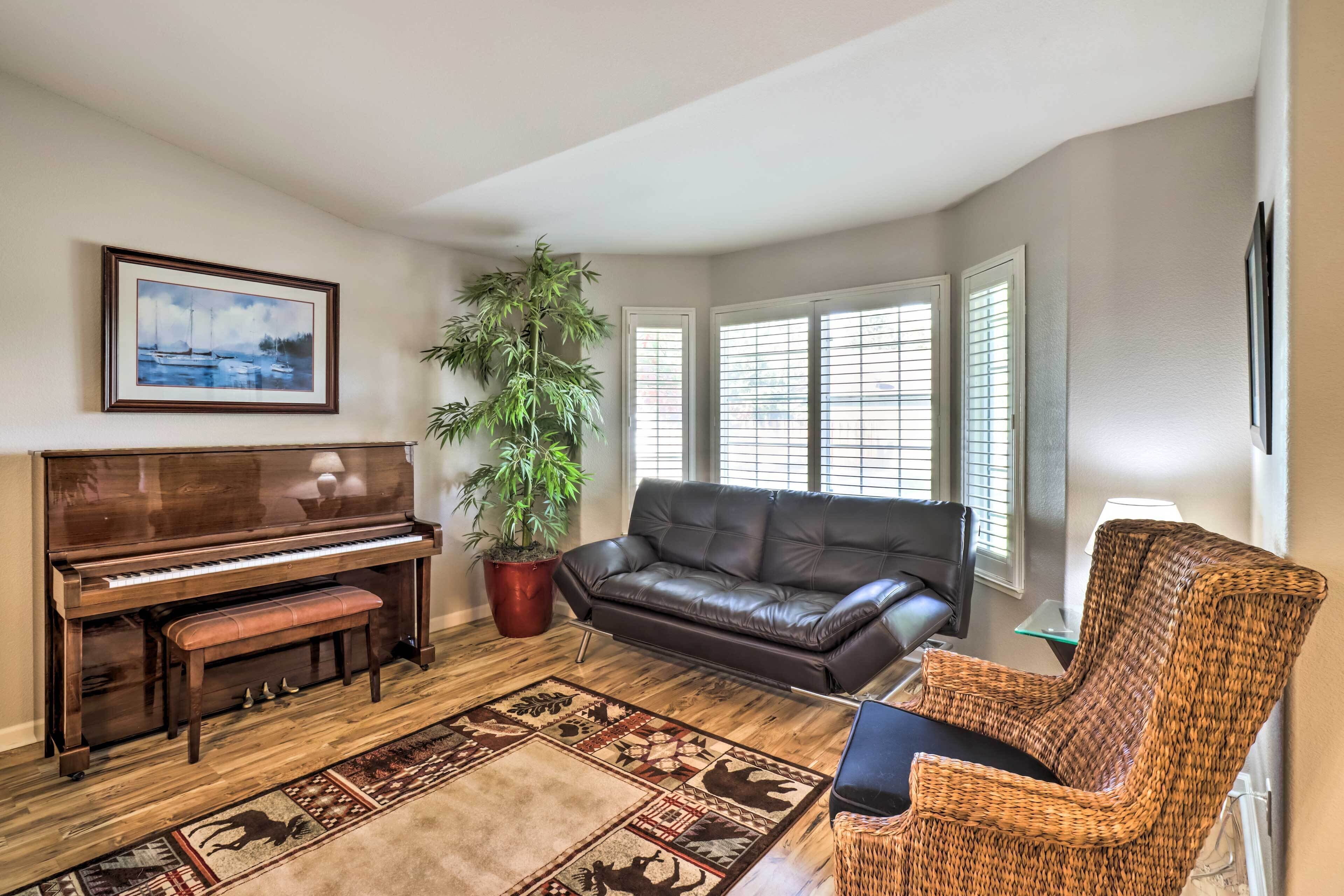 A living room with a piano, a large potted plant, a leather sofa, a wicker chair, and a patterned rug.