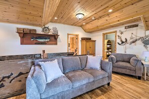 Ein gemütliches Wohnzimmer mit Holzbalkendecke, einem grauen Sofa und Holzboden.