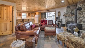 A cozy living room with leather sofas, a stone fireplace, and a kitchen in the background. - Rockaway Beach Hideaway w/ Hot Tub & Fireplace! (Rockaway Beach)