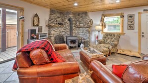 A cozy living room with leather sofas, a stone fireplace, and a large window. - Rockaway Beach Hideaway w/ Hot Tub & Fireplace! (Rockaway Beach)
