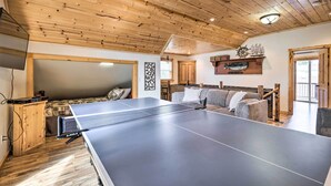 A ping pong table in a room with wooden ceilings and a bed with a plaid blanket. - Rockaway Beach Hideaway w/ Hot Tub & Fireplace! (Rockaway Beach)