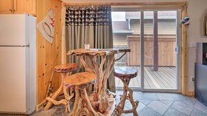 A wooden interior with a white refrigerator, a table with a unique design, and a sliding glass door leading to an outdoor deck. - Rockaway Beach Hideaway w/ Hot Tub & Fireplace! (Rockaway Beach)