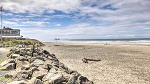 A beach with a rocky shoreline, a house with a balcony overlooking the beach, and the ocean in the background. - Rockaway Beach Hideaway w/ Hot Tub & Fireplace! (Rockaway Beach)