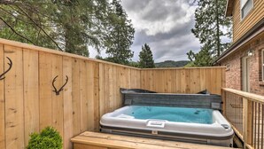 A wooden deck with a hot tub, a small potted plant, and a brick building in the background. - Rockaway Beach Hideaway w/ Hot Tub & Fireplace! (Rockaway Beach)