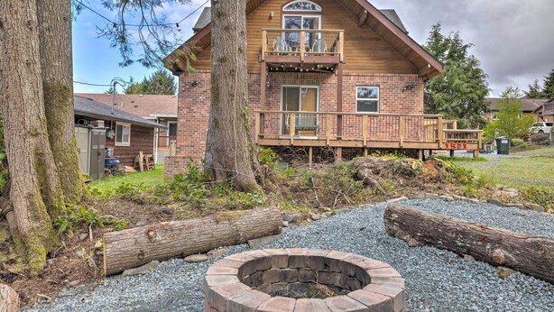 A two-story log cabin with a balcony, a fire pit, and a surrounding natural landscape. - Rockaway Beach Hideaway w/ Hot Tub & Fireplace! (Rockaway Beach)
