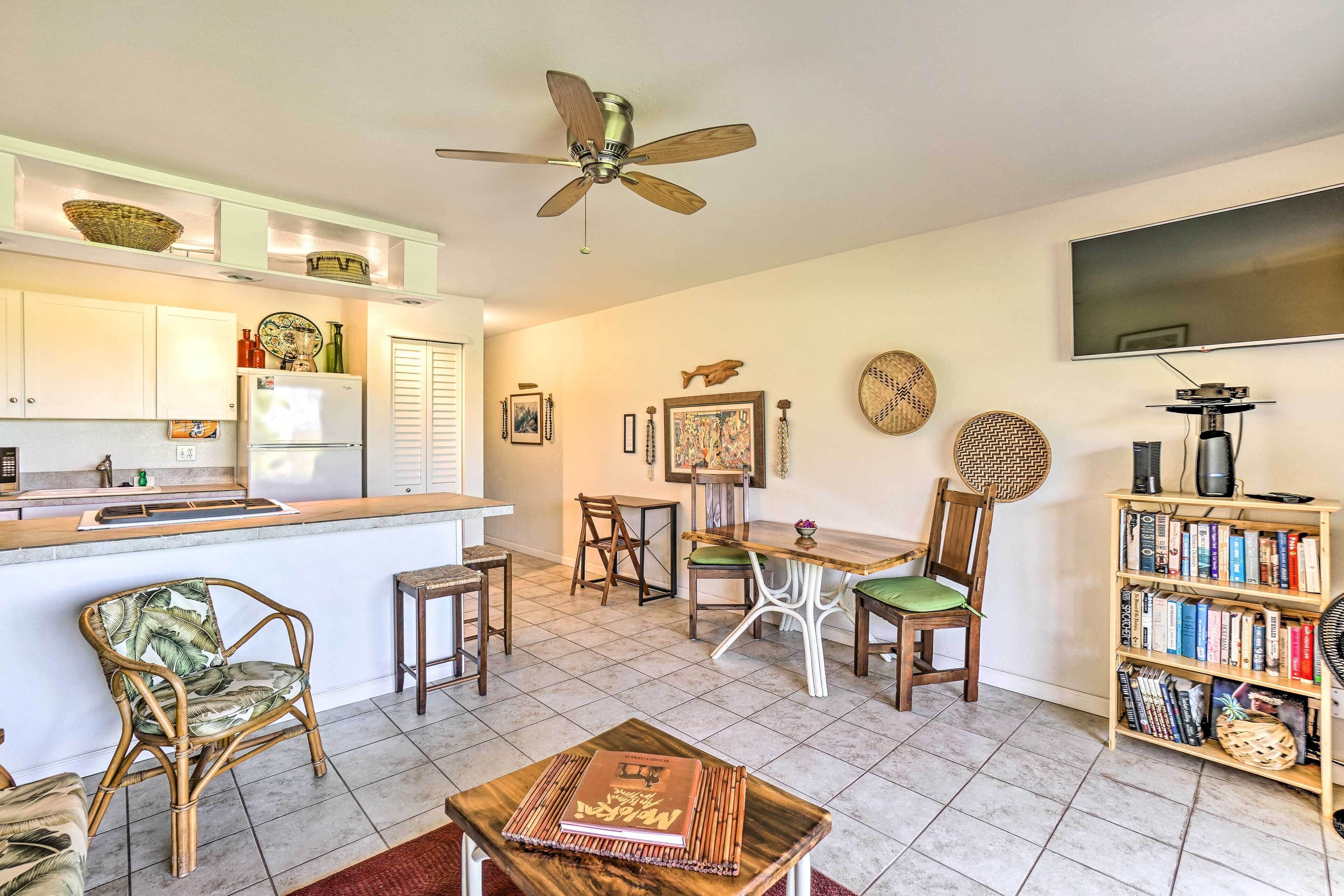 A modern kitchen with white cabinets, a wooden dining table, and a ceiling fan.