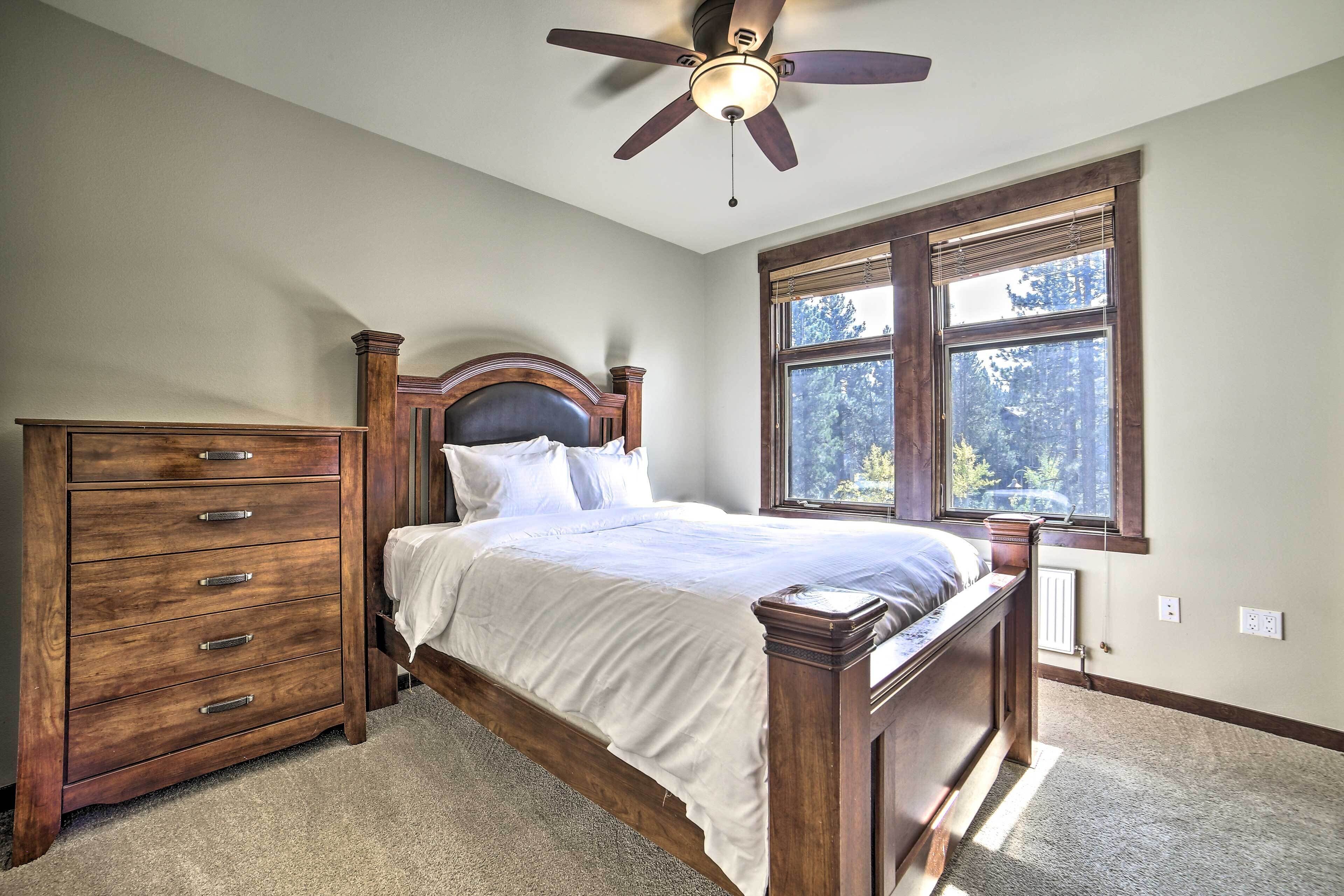 A bedroom with a wooden bed, a dresser, a ceiling fan, and a window with a view of trees.