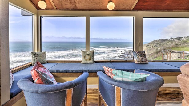 A cozy seating area with large windows overlooking the ocean, featuring cushioned chairs and decorative pillows.