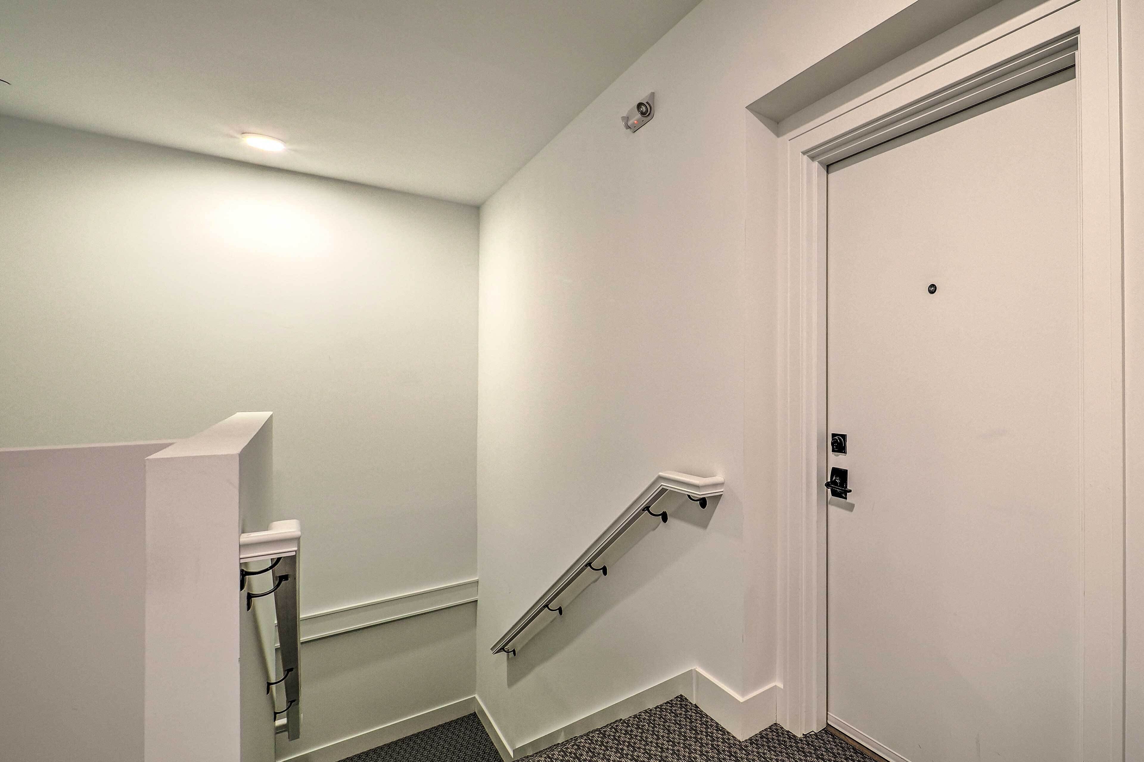 Un escalier étroit avec une rampe, une porte blanche et un petit luminaire au plafond.