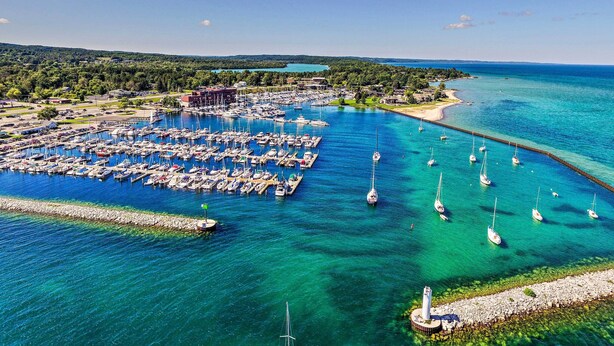 An aerial view of a marina with numerous boats docked, surrounded by lush greenery and a clear blue sea. - Downtown Traverse City Condo: 32 Mi to Ski Slopes! (Traverse City)