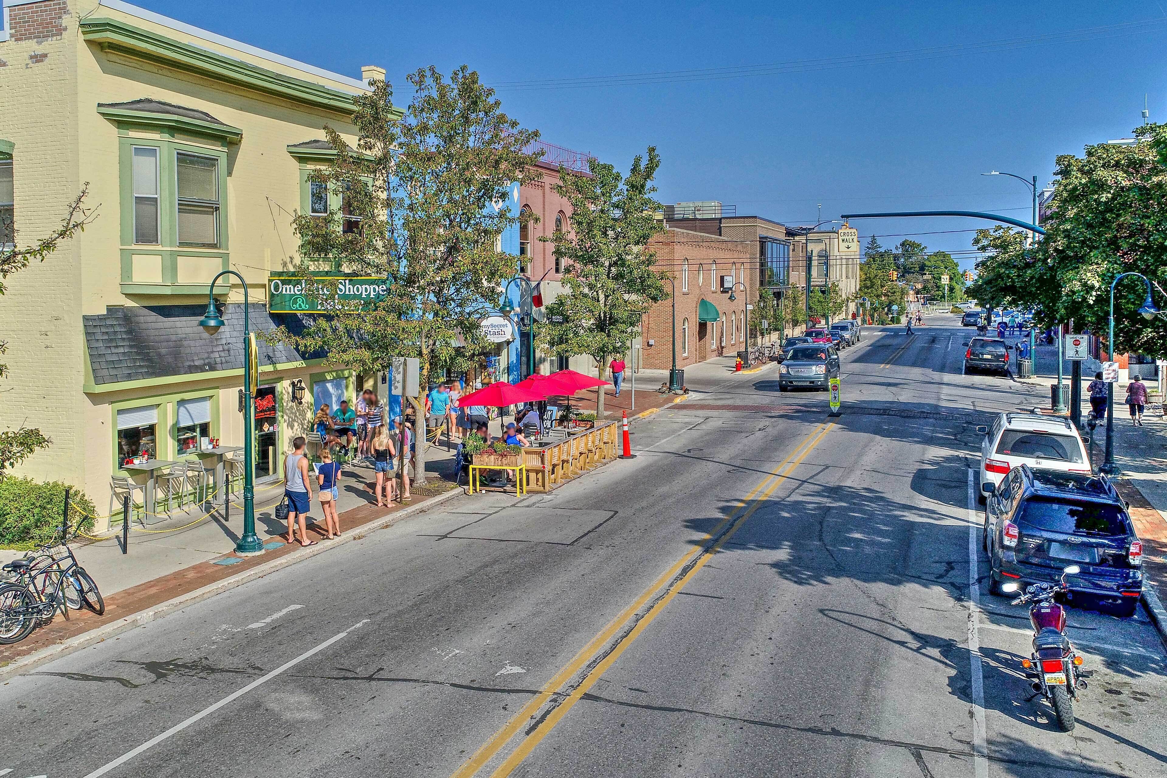 A street view with a row of shops, including a bakery and a cafe with outdoor seating.
