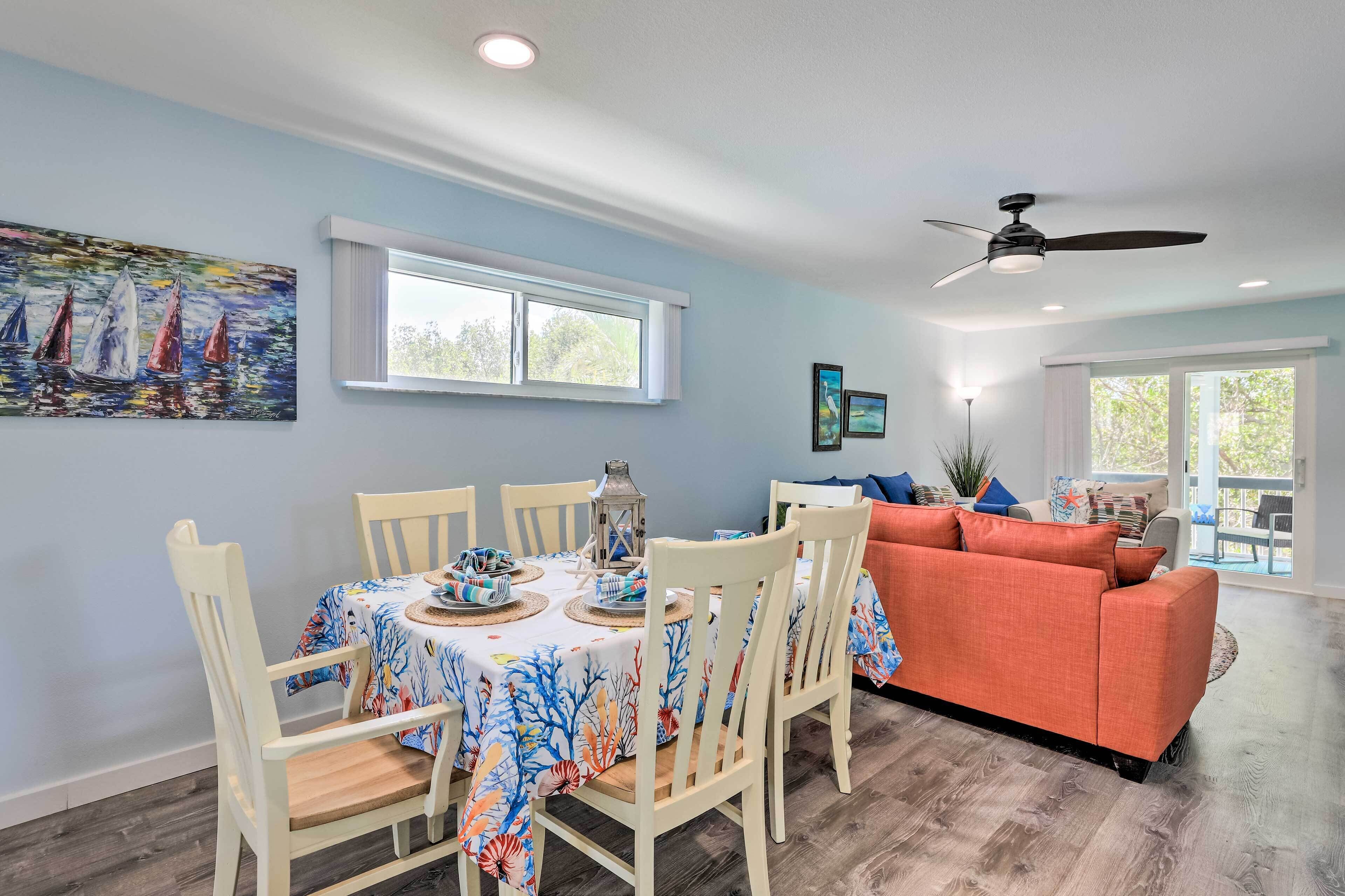 A dining area with a table set for four, white chairs, and a ceiling fan.