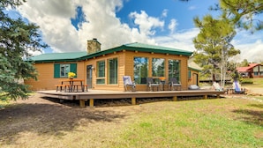 Eine Holzhütte mit grüner Dachdeckung, großen Fenstern und einer Terrasse mit Sitzgelegenheit.