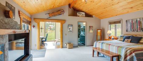 A spacious bedroom with a large bed, a wooden ceiling, a fireplace, and a view of the outdoors.