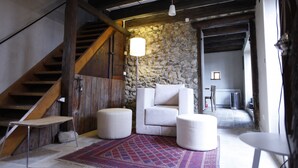 A rustic interior with a stone wall, wooden staircase, and a seating area with ottomans and a table. - Sessius 1622 (Cessy)