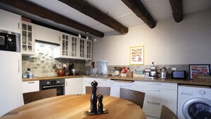 A kitchen with wooden cabinets, a stone backsplash, a wooden dining table, and a washing machine. - Sessius 1622 (Cessy)
