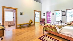 Un dormitorio espacioso con una cama grande, suelo de madera, un banco, una silla y un peluche.