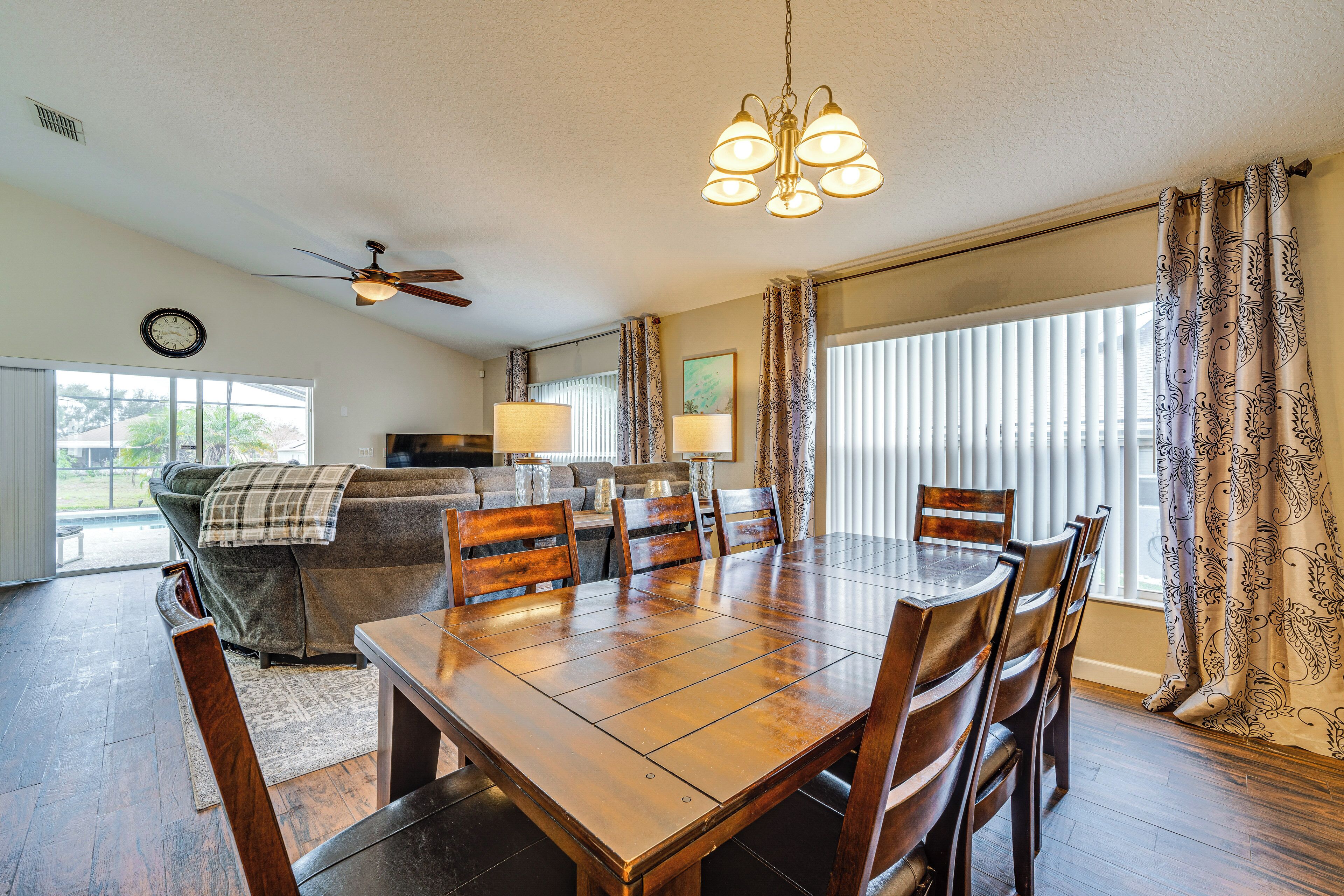 A dining area with a wooden table and chairs, a ceiling fan, and a chandelier.