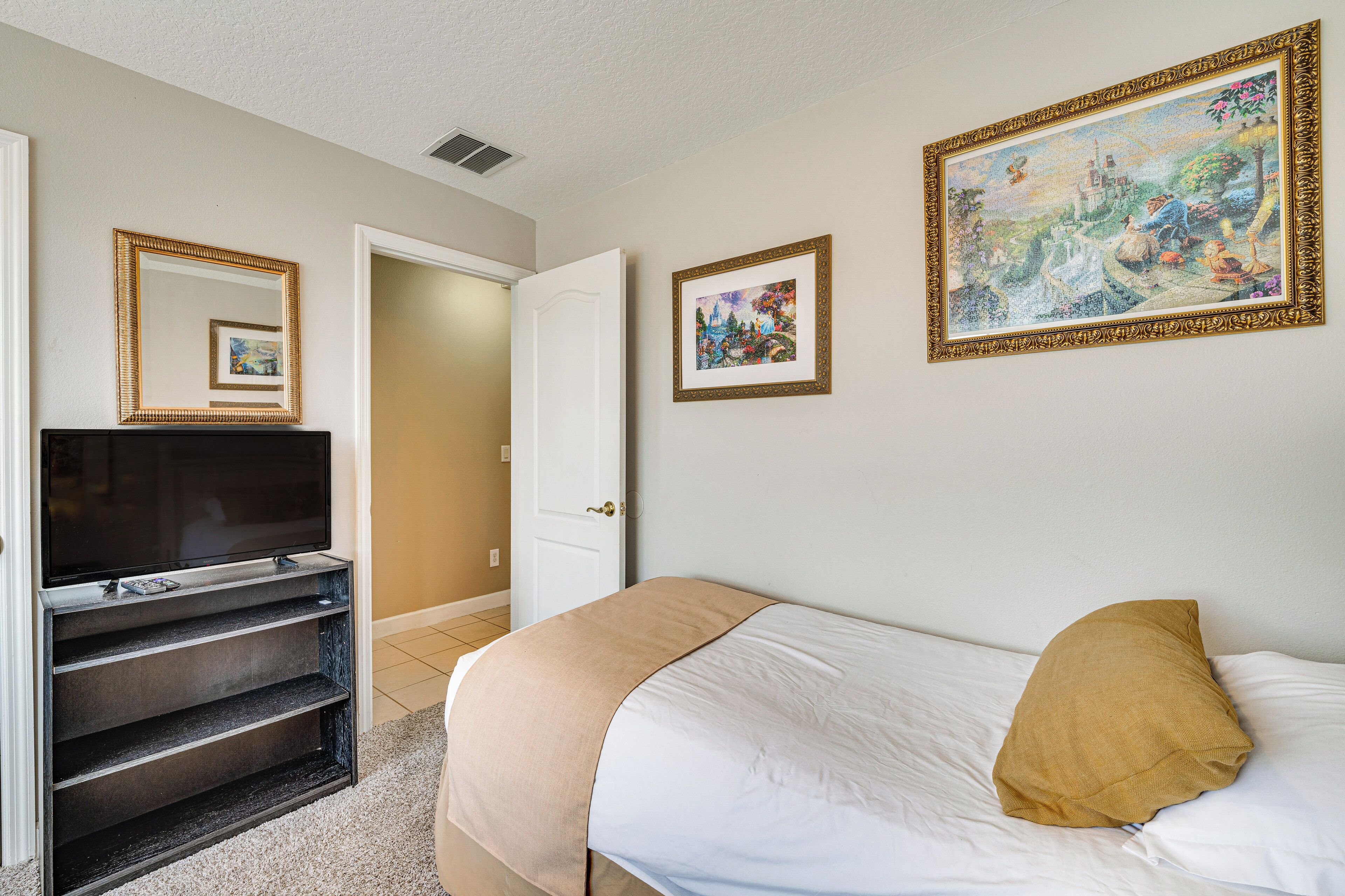 A hotel room with a bed, a television on a stand, a door, and two framed pictures on the wall.