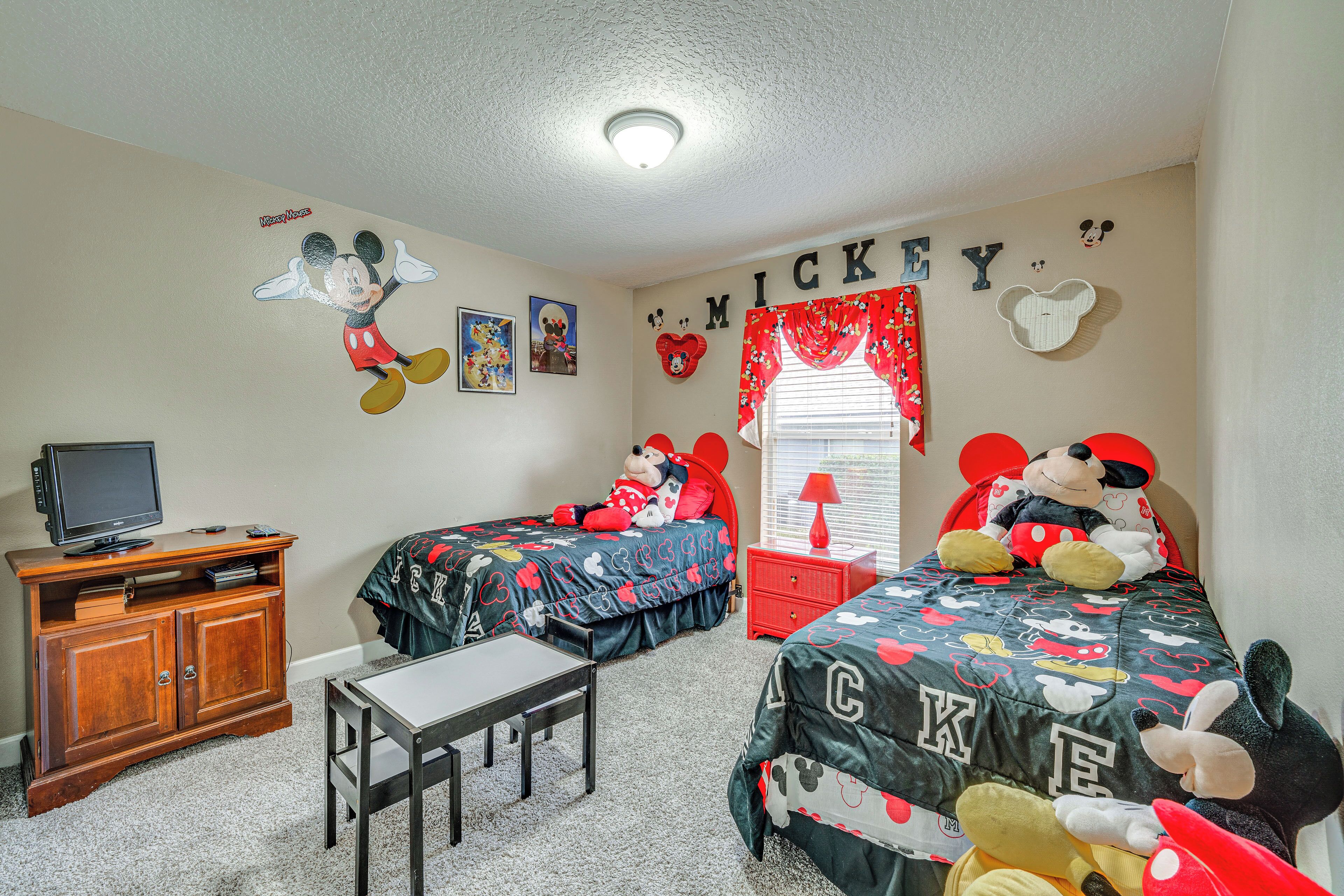 Un dormitorio infantil con dos camas, un televisor y decoración de Mickey Mouse.