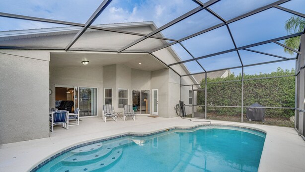 A swimming pool with a glass enclosure, a covered patio area with chairs, and a view of the surrounding greenery. - 11 Mi to Disney: Family-friendly Home in Davenport (Davenport)